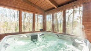 Un bain à remous dans un chalet en bois doté de grandes fenêtres donnant sur une forêt.