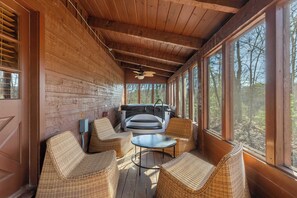 Eine Holzhütte mit Korbmöbeln, einem Whirlpool und großen Fenstern mit Blick auf den Wald.