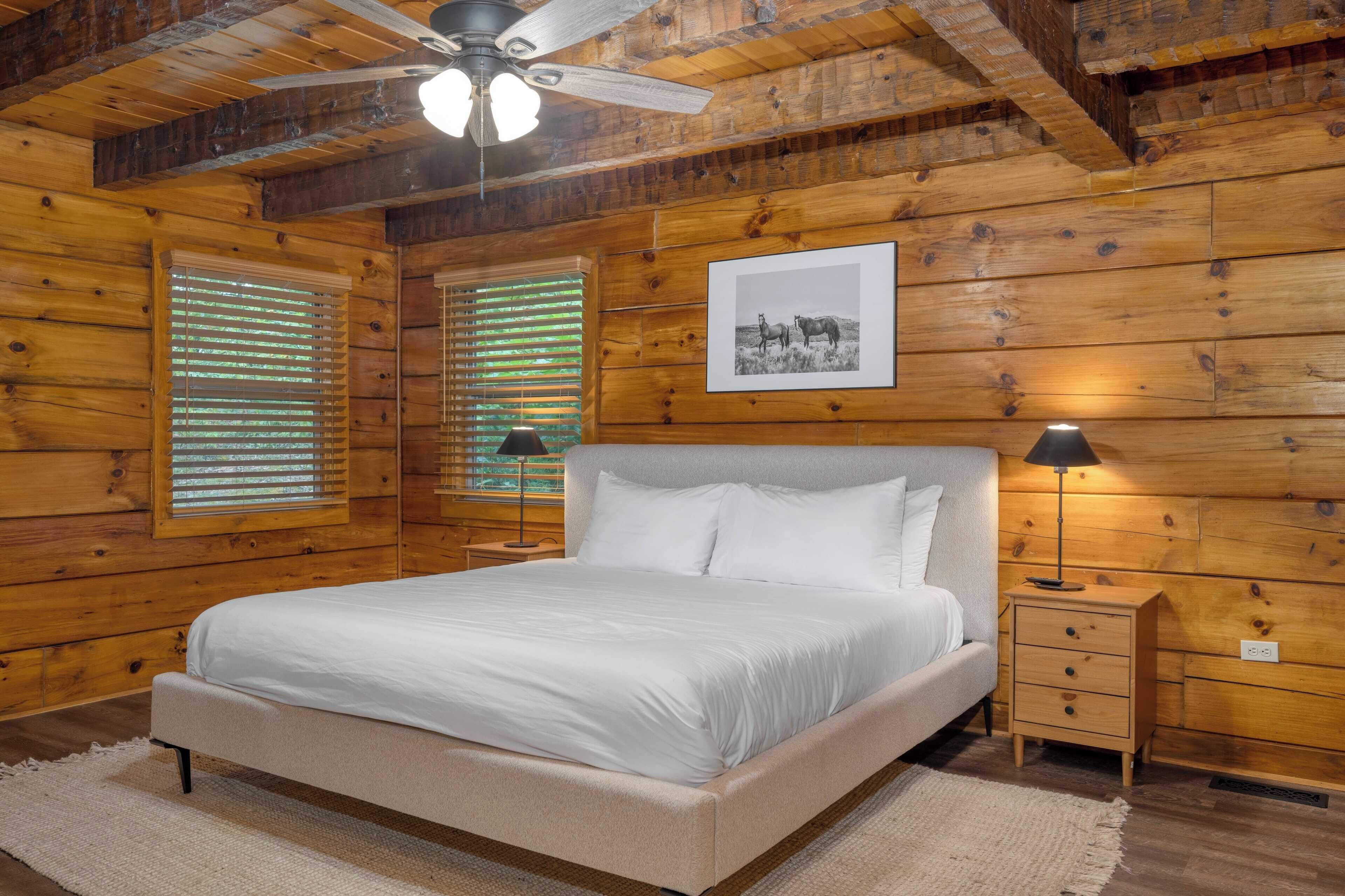A wooden cabin bedroom with a bed, nightstands, a ceiling fan, and a framed picture on the wall.