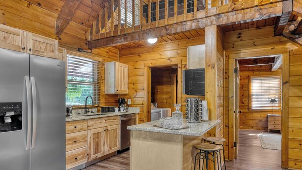 L’intérieur d’une cabane en bois comprend une cuisine équipée d’un réfrigérateur en acier inoxydable, de meubles de rangement en bois, d’un îlot central avec des tabourets et d’un coin repas.