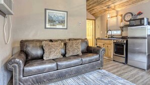 A cozy living room with a leather sofa, a framed landscape painting, and a kitchen with modern appliances. - Granite Peak. Near Mt-Rushmore National Memorial (Keystone)