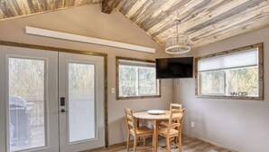 A dining area with a wooden table and chairs, a TV mounted on the wall, and large windows with blinds. - Granite Peak. Near Mt-Rushmore National Memorial (Keystone)