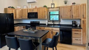 A modern kitchen with wooden cabinets, a black refrigerator, a dining table with chairs, and a built-in oven. - In the center of all the Black Hills has to offer, The Elkhorn Cabin with a Hot Tub (Keystone)