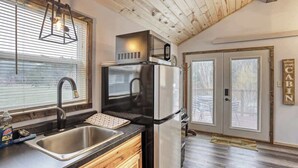 Una cucina con frigorifero in acciaio inossidabile, un lavello e mobili in legno. Si vede una finestra con persiane e una porta che dà su un'altra stanza.