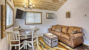 Un accogliente soggiorno con soffitto in legno, un divano in pelle marrone, un tavolo da pranzo con sedie e un baule vintage.