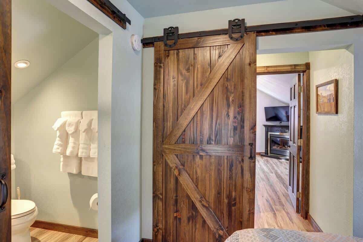 A room with a wooden sliding barn door, a white toilet, and a towel rack with towels.