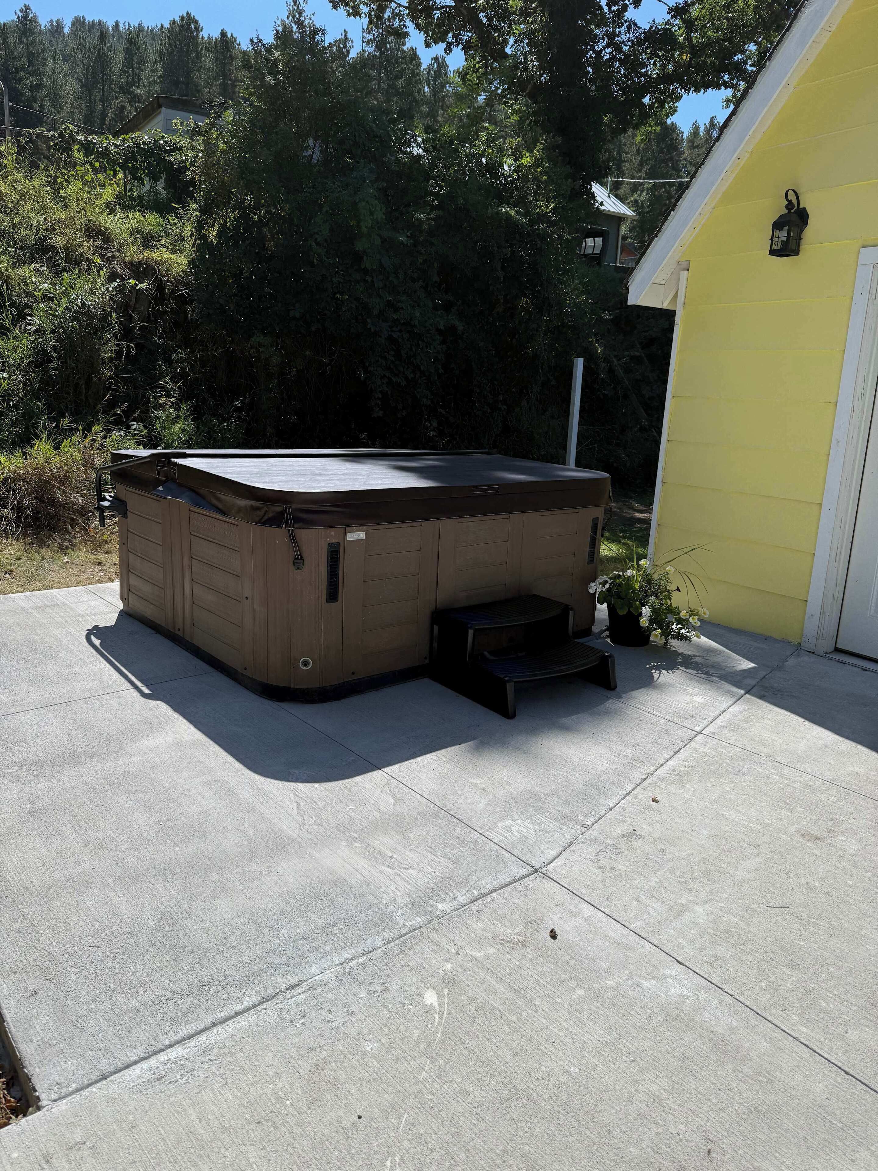 A hot tub with a wooden exterior, a step leading up to it, and a yellow building in the background.
