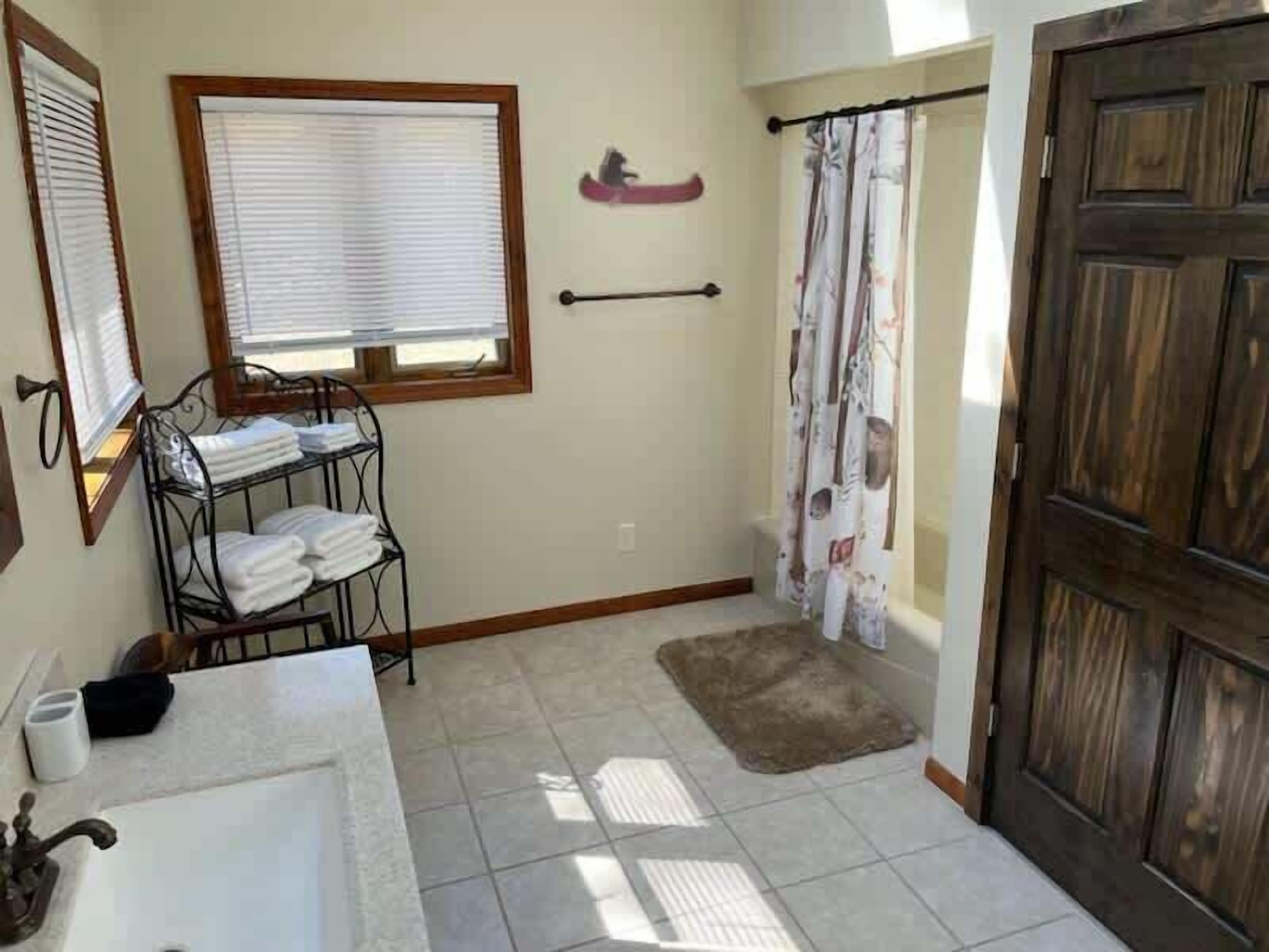 A bathroom with a sink, towel rack, shower curtain, and wooden door.