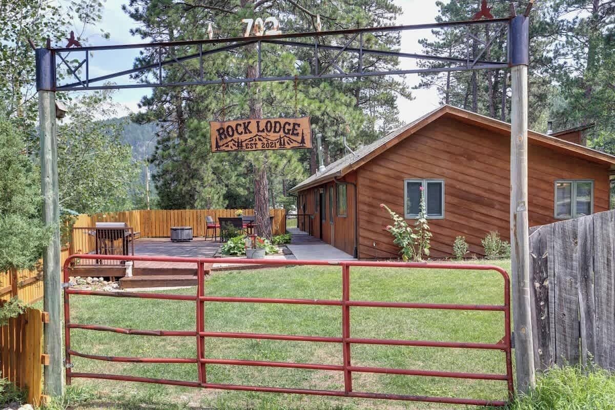 A wooden cabin labeled "Rock Lodge" with a fenced yard and a picnic table.