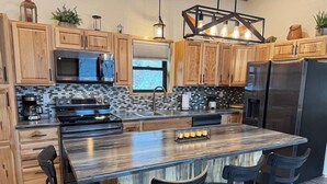 A modern kitchen with wooden cabinets, a large island with bar stools, stainless steel appliances, and a mosaic backsplash.