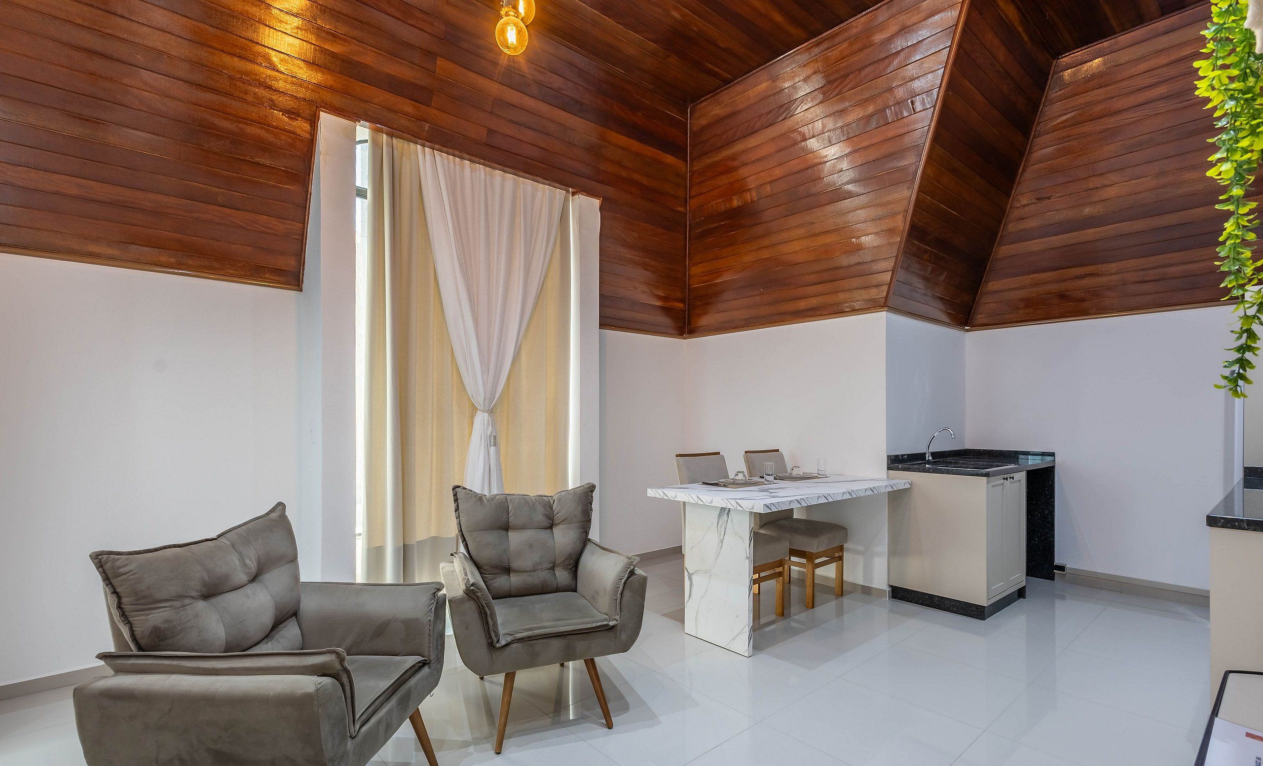 Una cucina moderna con un piano di lavoro in marmo, soffitto in legno e un'area pranzo con due divani grigi e un tavolo.