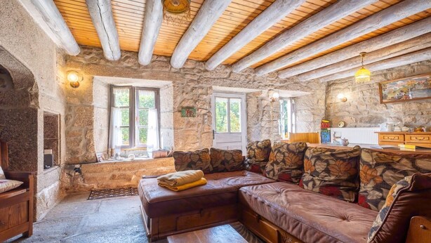 A rustic stone interior with a wooden ceiling, a leather sofa, a wooden table, and a stone fireplace.