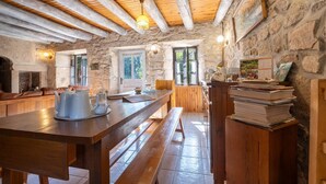 A rustic kitchen with stone walls, wooden beams, and a long wooden table with benches.