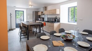 A modern kitchen with wooden cabinets, a dining area with a table set for four, and a view of greenery outside. - Lozeret vacation rentals (CUBIERES)