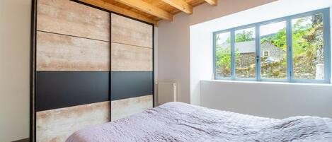 A bedroom with a bed, a wooden ceiling, a window with a view of greenery, and a sliding door.