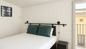 Un dormitorio con cama, mesita de noche y vistas al balcón exterior.
