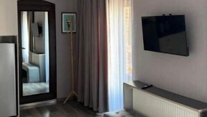 Ein modernes Hotelzimmer mit einem großen Spiegel, einem flachbildfernseher an der Wand, einer Bank und Blick auf die Stadt durch große Fenster.