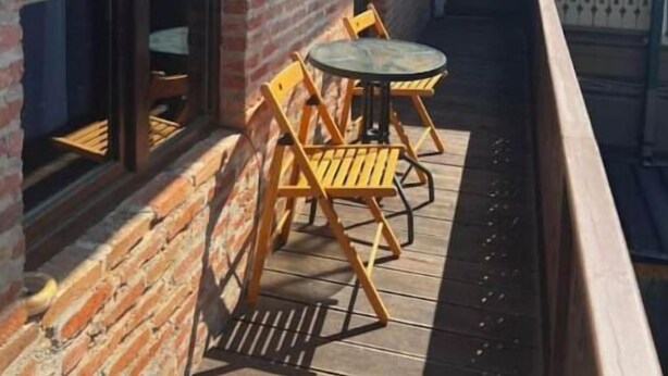 Ein überdachter Außenbereich mit Ziegelwand, Holzterrasse und rundem Tisch mit Stühlen.