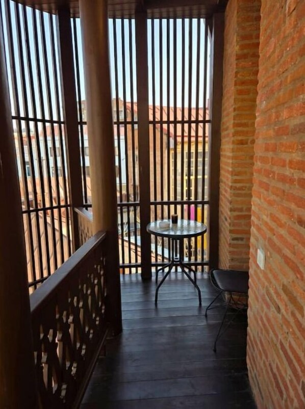 A balcony with a glass table and chairs, a brick wall, and a view of buildings in the background. - Art Nouveau 18 Exclusive (Chugureti)