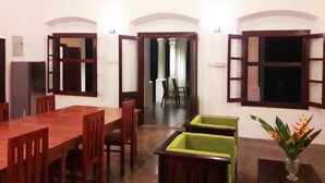 A dining area with a wooden table and chairs, a small green bench, and a vase with flowers. - Villa Primrose Cottage (Galle)