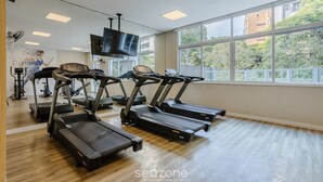 Een sportschool met loopbanden, trainingsfietsen en een televisie aan de muur.