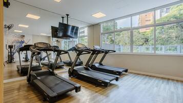 Un gimnasio con cintas de correr, bicicletas estáticas y un televisor en la pared.