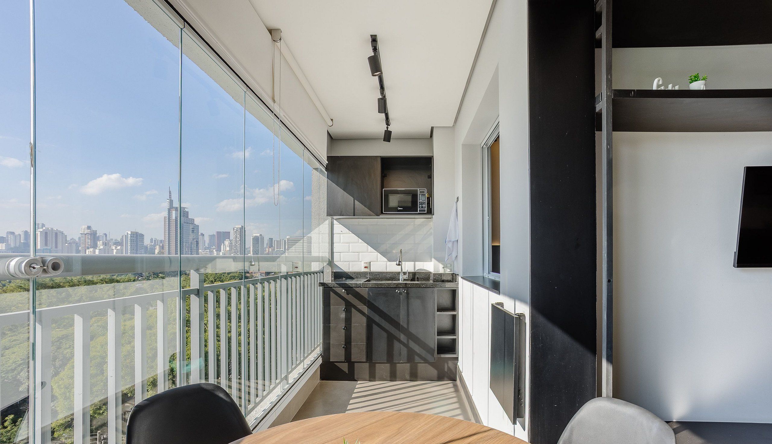 Un balcón con vista a la ciudad, una pequeña cocina y un comedor con mesa y sillas.
