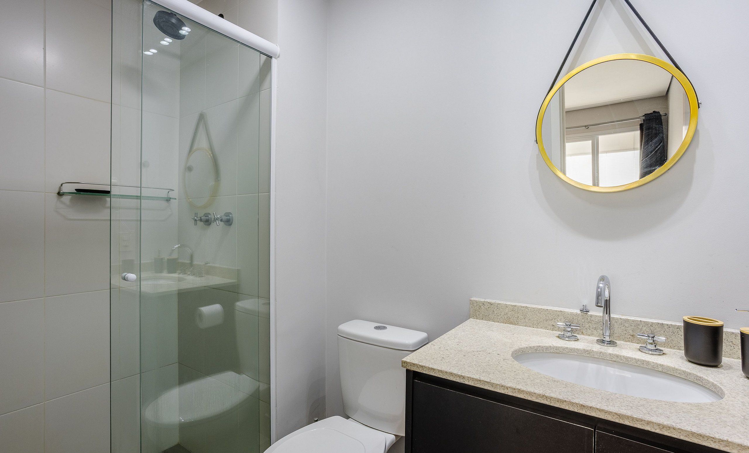 Un baño moderno con ducha envuelta en vidrio, inodoro y lavamanos con encimera de granito.