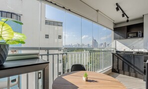 A modern kitchen with a view of the city skyline, a dining area with a table and chairs, and a balcony with a railing. - Apt w/ Gourmet Balcony 190m From the Metro Wal0714 (São Paulo)