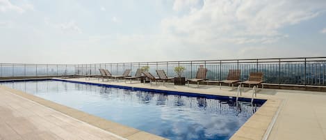 A rooftop pool area with lounge chairs and a clear view of the city skyline.
