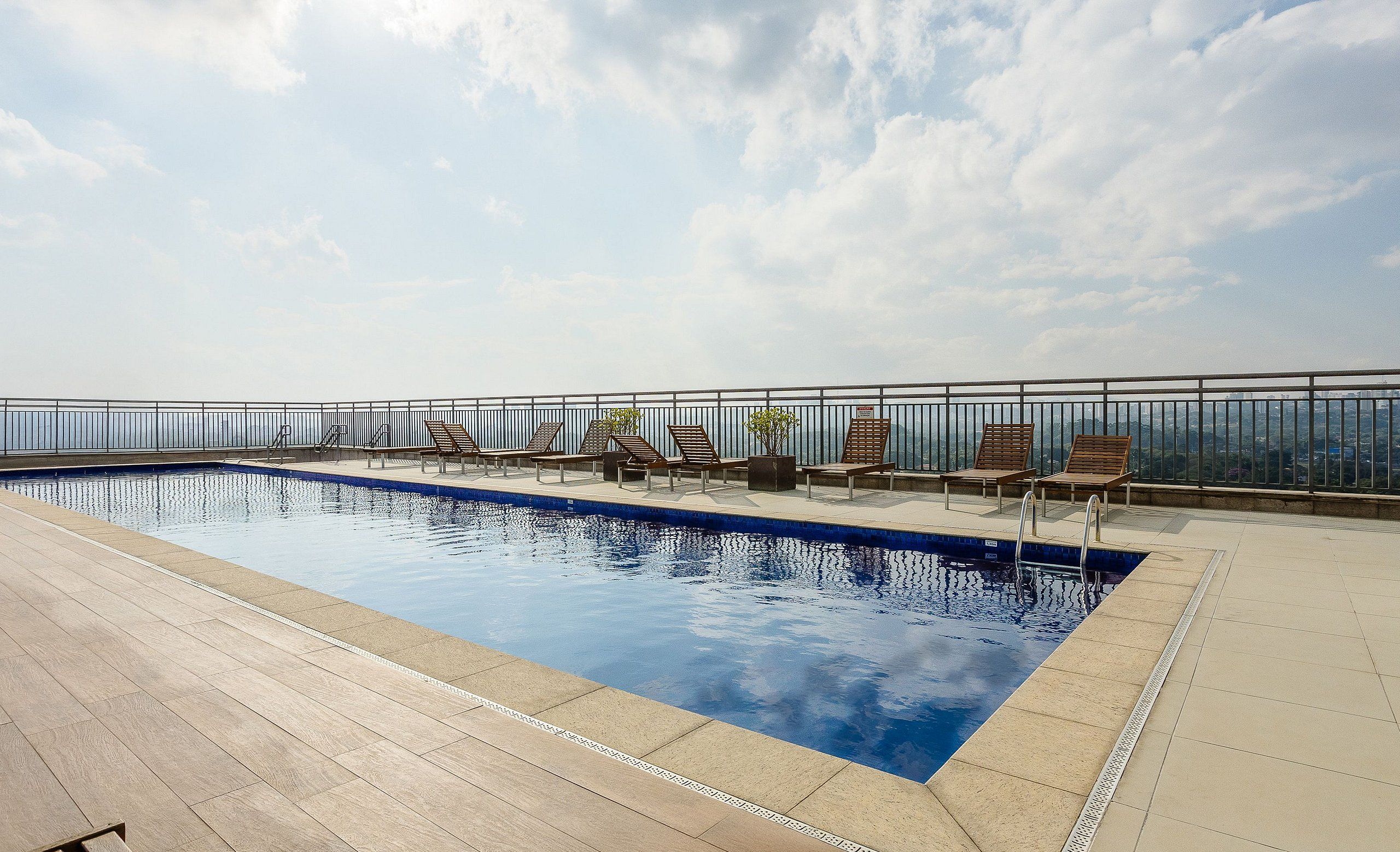 Un área de piscina en la azotea con sillones de descanso y una vista despejada del horizonte de la ciudad.