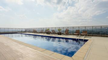 Un área de piscina en la azotea con sillones de descanso y una vista despejada del horizonte de la ciudad.