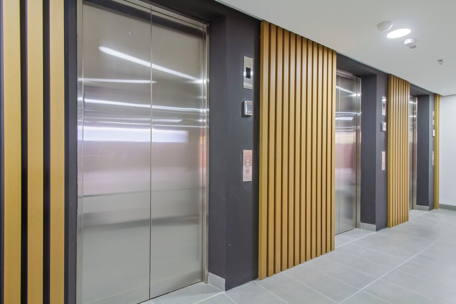 A modern elevator with a metallic finish, a control panel, and a wall with vertical wooden slats.