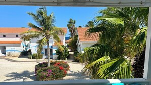A view of a courtyard with palm trees, a flower bed, and buildings with red-tiled roofs.