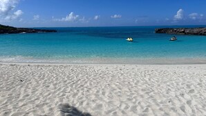 Una platja amb aigua turquesa cristal·lina, dues petites embarcacions i afloraments rocosos.