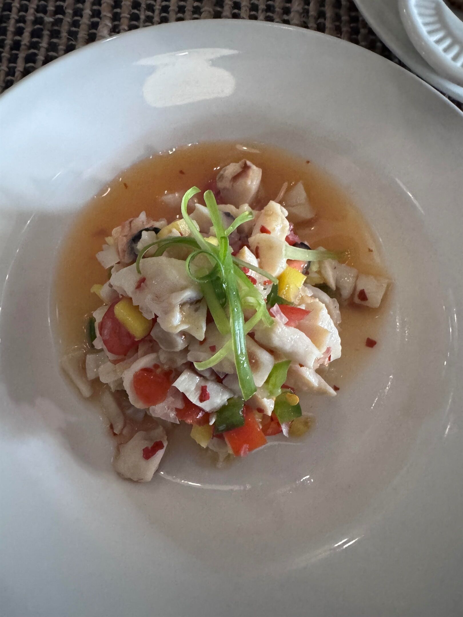 Un plato blanco con un plato de mariscos, que incluye pescado en cubos y verduras, con una salsa de color claro.