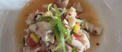 Un plato blanco con un plato de mariscos, que incluye pescado en cubos y verduras, con una salsa de color claro.