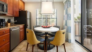 A modern kitchen with wooden cabinets, a stainless steel refrigerator, a dishwasher, and a round dining table with four chairs. - 2-bedroom Resort Villa in Orlando-Universal, Disney, Epcot (Orlando)