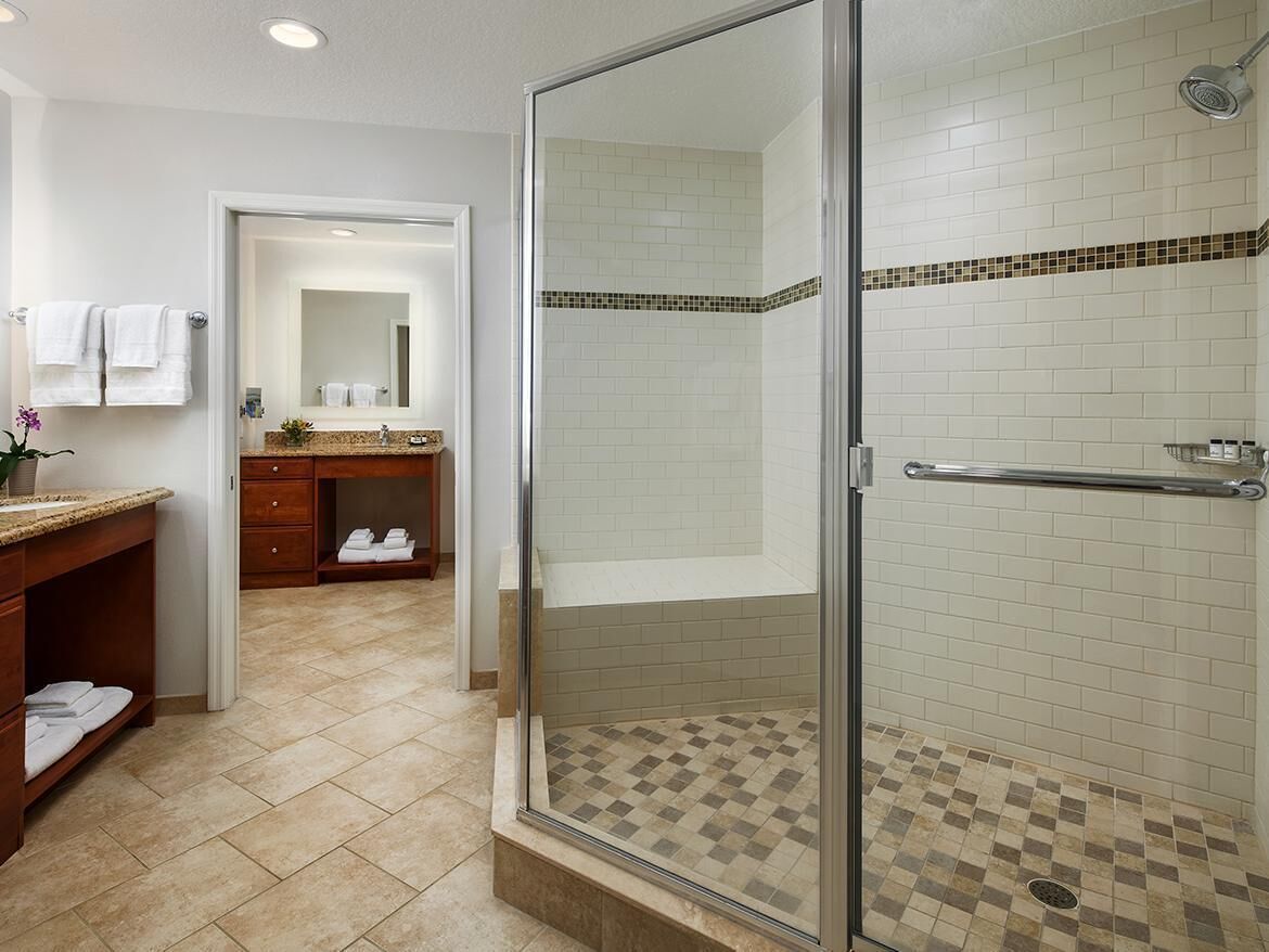 Un baño moderno con ducha de vidrio, tocador con espejo y piso de baldosas.