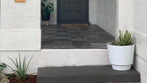 A house entrance with a dark door, a wooden mailbox with numbers, and two potted plants.
