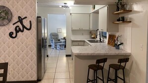 A modern kitchen with white cabinetry, a marble countertop, and a bar area with stools.
