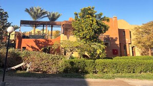 A traditional building with a wooden lattice structure, surrounded by greenery and palm trees.