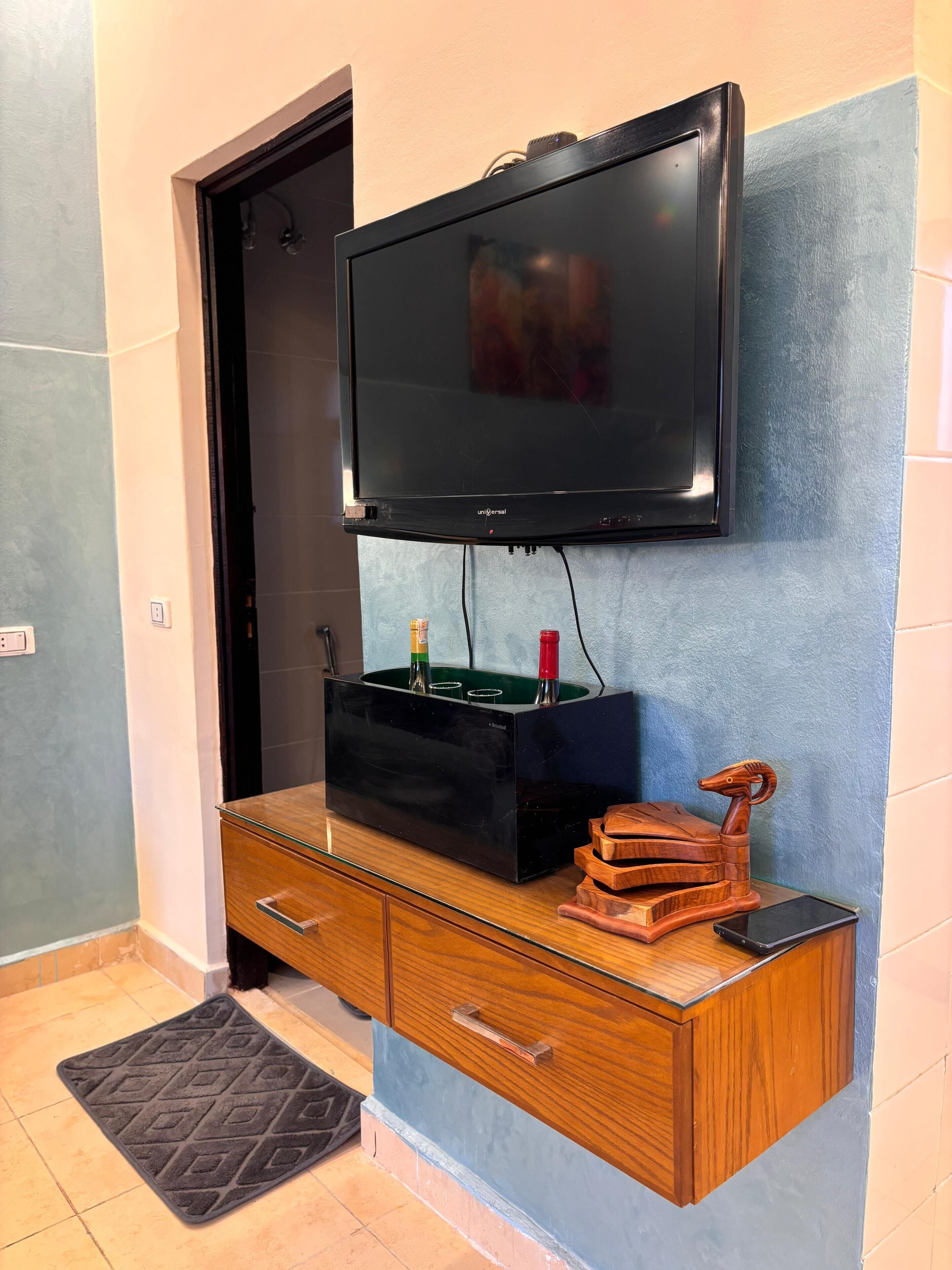 A flat-screen TV mounted on a wall above a wooden cabinet with drawers.