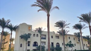 A building with multiple balconies, surrounded by palm trees and greenery.