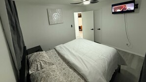 A bedroom with a bed, a ceiling fan, a TV, and a door leading to another room.