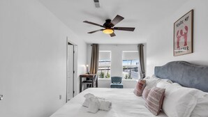 A hotel room with a bed, a desk, a chair, a ceiling fan, and a window with curtains. - Professionally Managed | Walk to Beach (Seaside Heights)