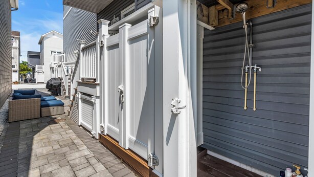 A narrow outdoor corridor with white doors, a covered patio area with wicker furniture, and a grey garage door. - Professionally Managed | Walk to Beach (Seaside Heights)