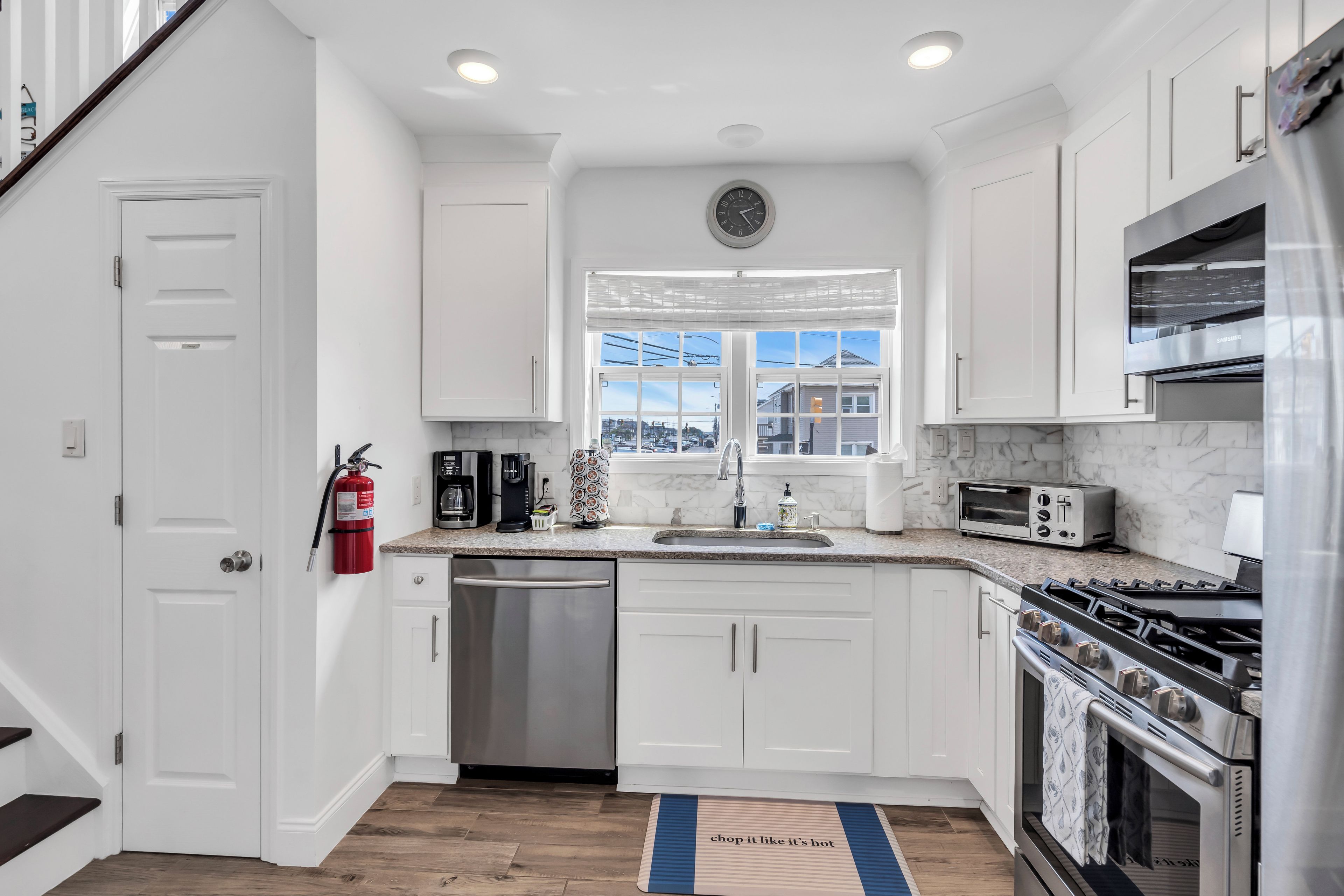 Una cocina moderna con armarios blancos, electrodomésticos de acero inoxidable y ventana con vista a una zona residencial.