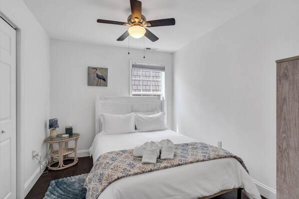 A bedroom with a bed, a ceiling fan, a window, and a bedside table with a lamp. - Professionally Managed | Walk to Beach (Seaside Heights)