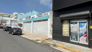 A street view with a black building featuring a large digital screen, parked cars, and a blue building with a sign for a Subway restaurant in the background. - HOSTEL OF SANTURCE (San Juan)